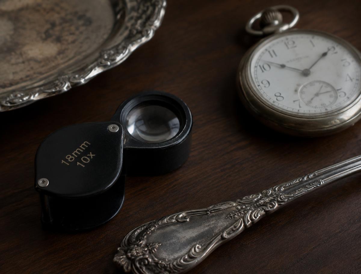 Jeweler's loupe beside antique silver and a pocket watch
